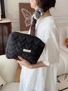 Quilted heart pattern black makeup clutch with zipper closure held by a model
