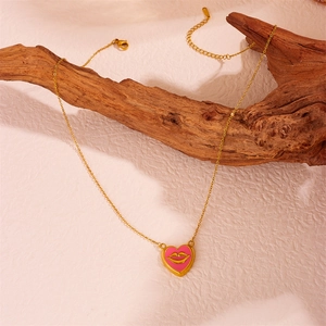 Gold chain necklace with pink heart lip pendant placed on a textured piece of driftwood