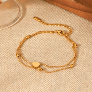 Detail of 18K gold-plated double-layer heart anklet with beads on textured fabric
