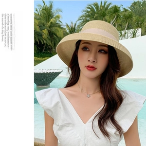 Elegant wide-brim straw sun hat featuring a light pink ribbon bow against a pool background