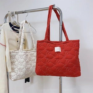 Detail of red and cream quilted tote bags with rabbit embroidery and label on hangers