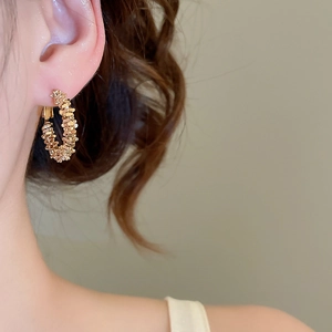 Detail of textured golden hoop earrings with woven metallic scales on model