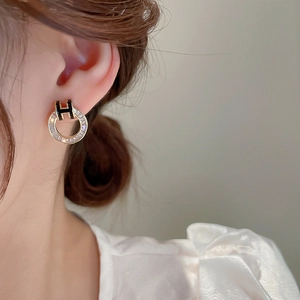 Close-up of gold-plated hoop earring with crystal pavé and black enamel H-shaped detail