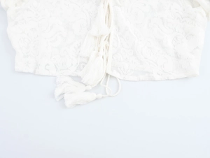 Close-up of white lace blouse featuring delicate floral embroidery and tie-up tassel detail