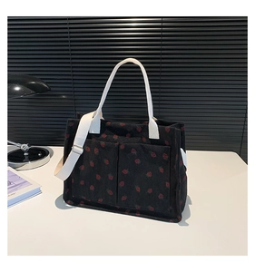 Close-up of black corduroy tote bag with red strawberry pattern and white straps