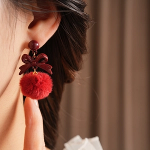 Close-up of red bow and fluffy pom-pom earrings on a model for a vintage aesthetic