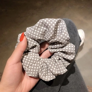 Hand holding a gray scrunchie with white polka dots made of soft fabric texture