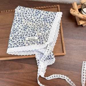 Detail of blue floral cotton headscarf with white lace trim and 100% cotton label