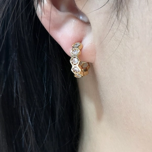Macro view of 18K gold honeycomb earrings with inlaid zircons worn on the ear