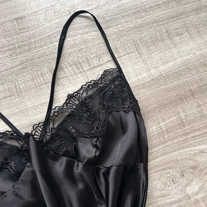 Elegant black satin camisole with floral lace neckline and thin straps on wood background