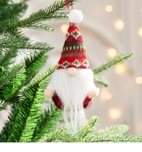 Close-up of a knitted Christmas gnome ornament hanging on a pine tree with warm bokeh light