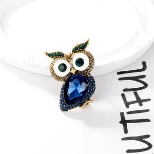 Detail of owl brooch featuring a blue water-drop gem and green crystal accents