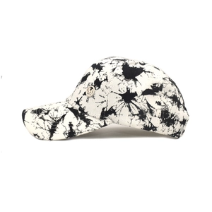 Detail view of tie-dye baseball cap with silver M logo emblem and breathable cotton fabric