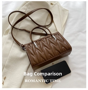 Detail view of brown pleated matte leather handbag with dual handles and phone for scale
