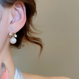 Close-up of elegant silver bow pearl drop earrings with sparkling zircon on model
