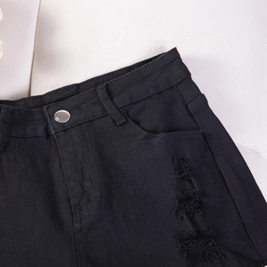Vista macro di pantaloncini di denim neri a vita alta con dettagli strappati e bottone in metallo
