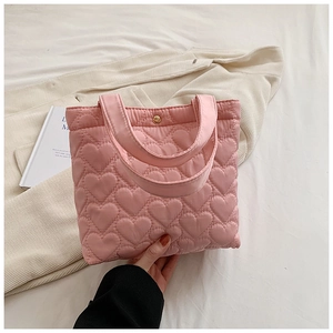 Close-up of pink heart-quilted puffer tote bag held by hand in a soft aesthetic setting