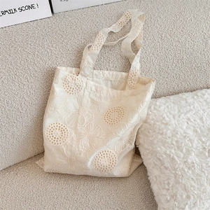 Detail of floral embroidery and hollow cut-outs on off-white canvas tote bag