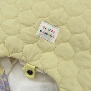 Détail d'un sac fourre-tout matelassé jaune avec étiquette tissée et bouton pression