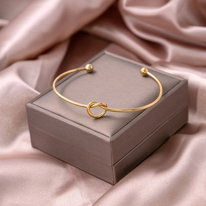 Detail of a polished gold knot open bangle on luxury silk champagne fabric