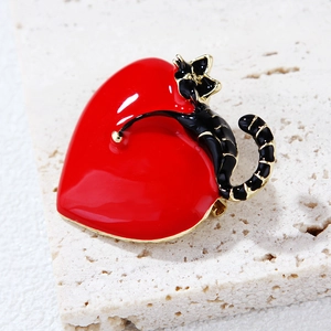Detail of a black cat on a red heart enamel brooch with gold edges on white stone