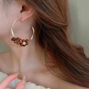 Detail of C-shaped golden hoop earring with woven sandalwood beads on a model