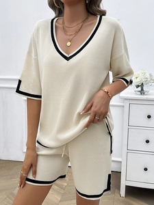 Detail of beige knit two-piece set featuring V-neck top with stylish black striped edges