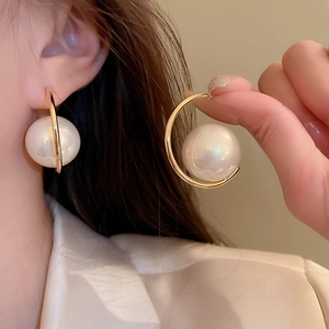 Close-up of elegant gold C-shaped hoop earring featuring a large white pearl bead