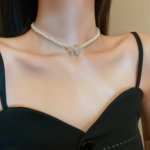 Detail of elegant bow pendant with inlaid rhinestones on a white faux pearl necklace