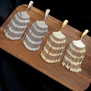 Detailed macro view of gold and silver fan-shaped metal tassel earrings on dark wood
