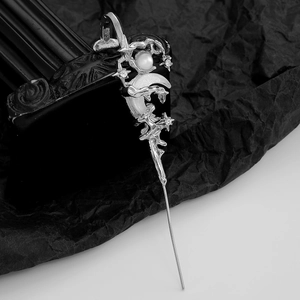 Macro detail of silver hair pin with star and moon charms and white pearls on black stone