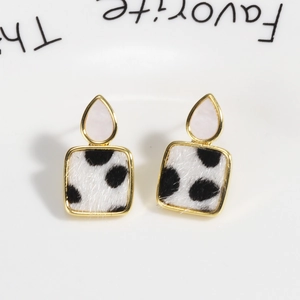 Macro detail of teardrop earrings with gold borders and black and white spotted fur textures