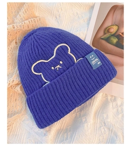 Close-up of blue-purple knitted beanie with bear embroidery and smile face woven label