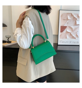 Detail of emerald green crocodile textured leather handbag with gold hardware and woven handle