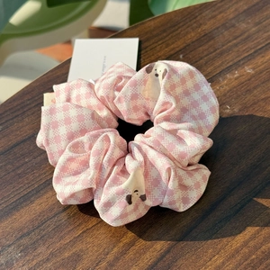 Detailed view of pink plaid scrunchie with cute dog pattern on a dark wood table