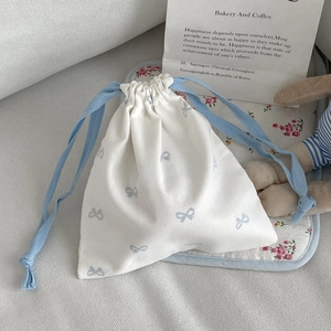 Close-up of white cotton drawstring bag with blue bow prints and matching ribbons