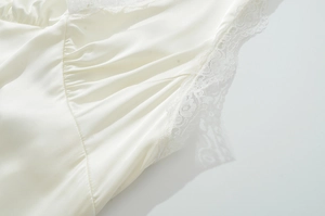 Detail eines cremefarbenen Satin-Kleides mit zarter Spitze und glatter Seidentextur