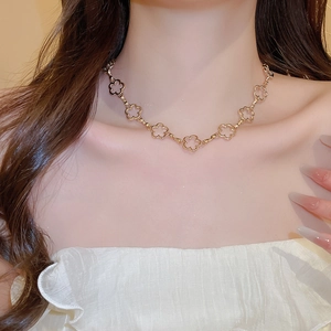 Detail of a gold clover hollow necklace worn by a model showcasing the tassel chain design