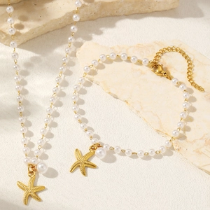 Starfish pearl jewelry set featuring golden charms and white beads on beach sand