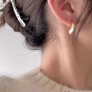 Close-up of elegant gold wide C-shaped hoop earrings worn by a model in a minimal style