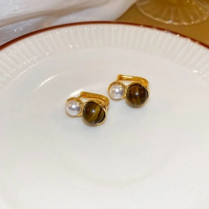 Detail of gold earrings with white pearl and tiger eye beads on ceramic tray