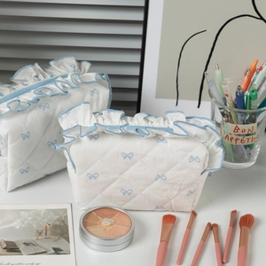 Detailed view of white quilted cosmetic bag with blue bow print and ruffled edge