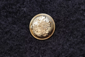 Macro detail of golden embossed heraldic metal buttons on a black wool coat fabric