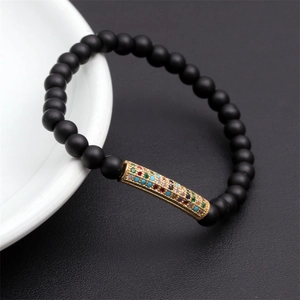 Macro shot of matte black beads bracelet with a gold-plated colorful zircon curved tube
