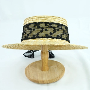 Detail of elegant boater straw hat featuring a wide black floral lace ribbon on a wooden stand