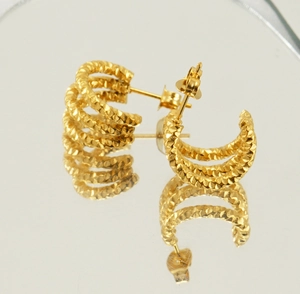 Détail macro de boucles d'oreilles créoles torsadées dorées à trois couches sur miroir