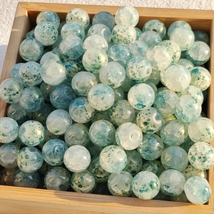 Macro shot of green and white marble pattern glass beads in a square wooden tray