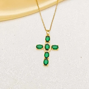 Detail of gold cross necklace featuring oval emerald green stones and zircon accents