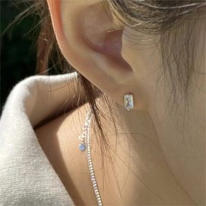 Close-up of minimalist rectangular crystal stud earring worn on ear with silver setting