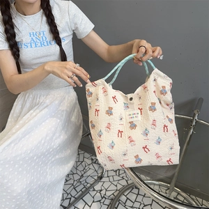 Detail of seersucker tote bag with cartoon bear print and blue woven handles on model